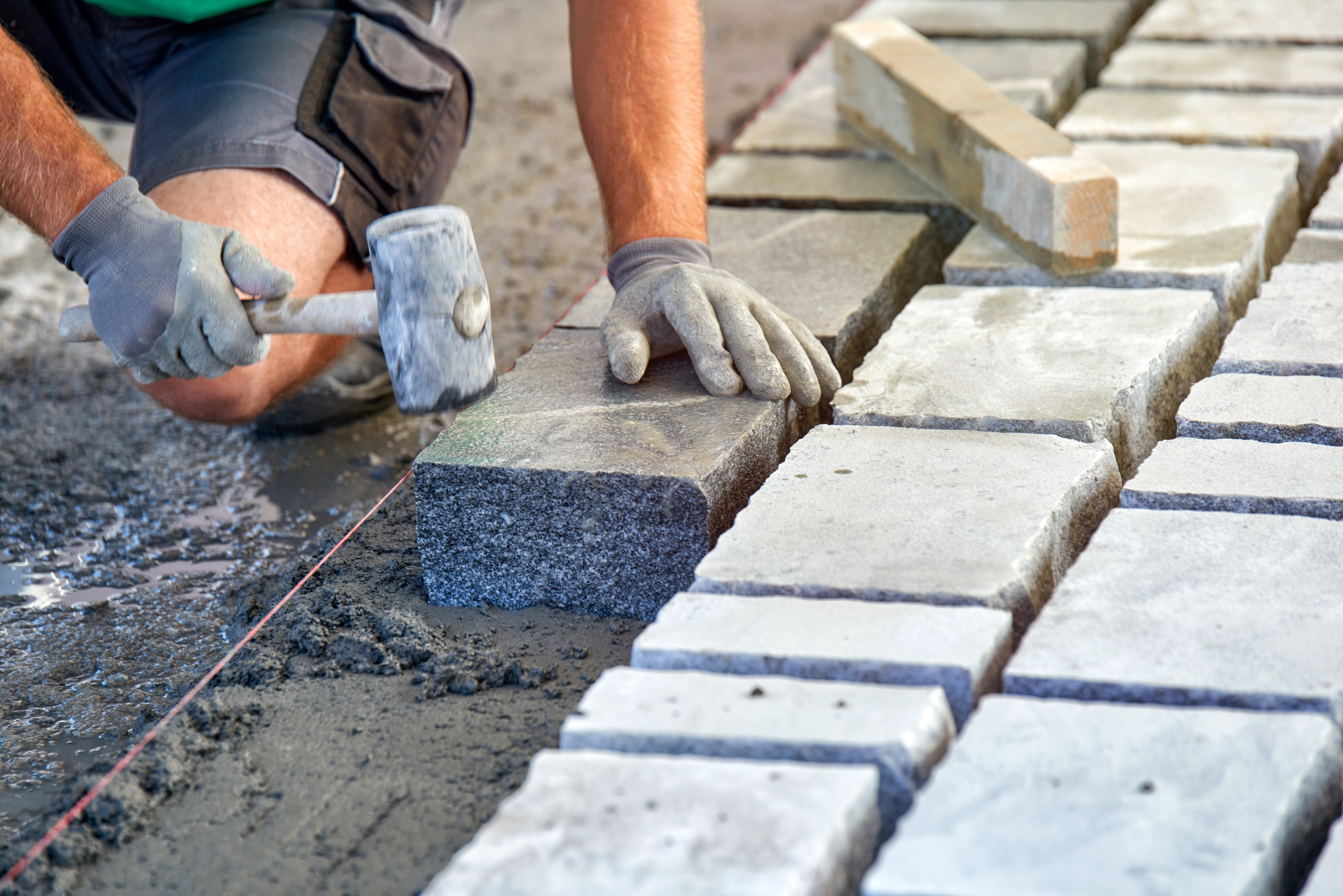 a workman's gloved hands use a hammer to place stone pavers. wor
